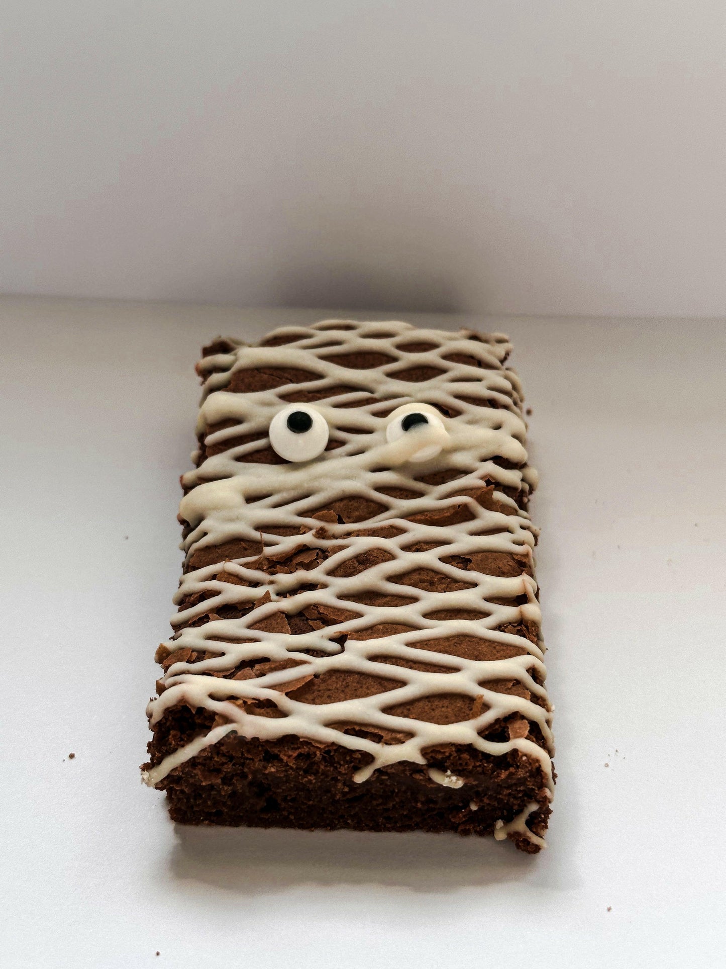 A Halloween-themed brownie transformed into a charming mummy, wrapped in white chocolate bandages and adorned with spooky candy eyes, perfect for a frightfully delicious treat."